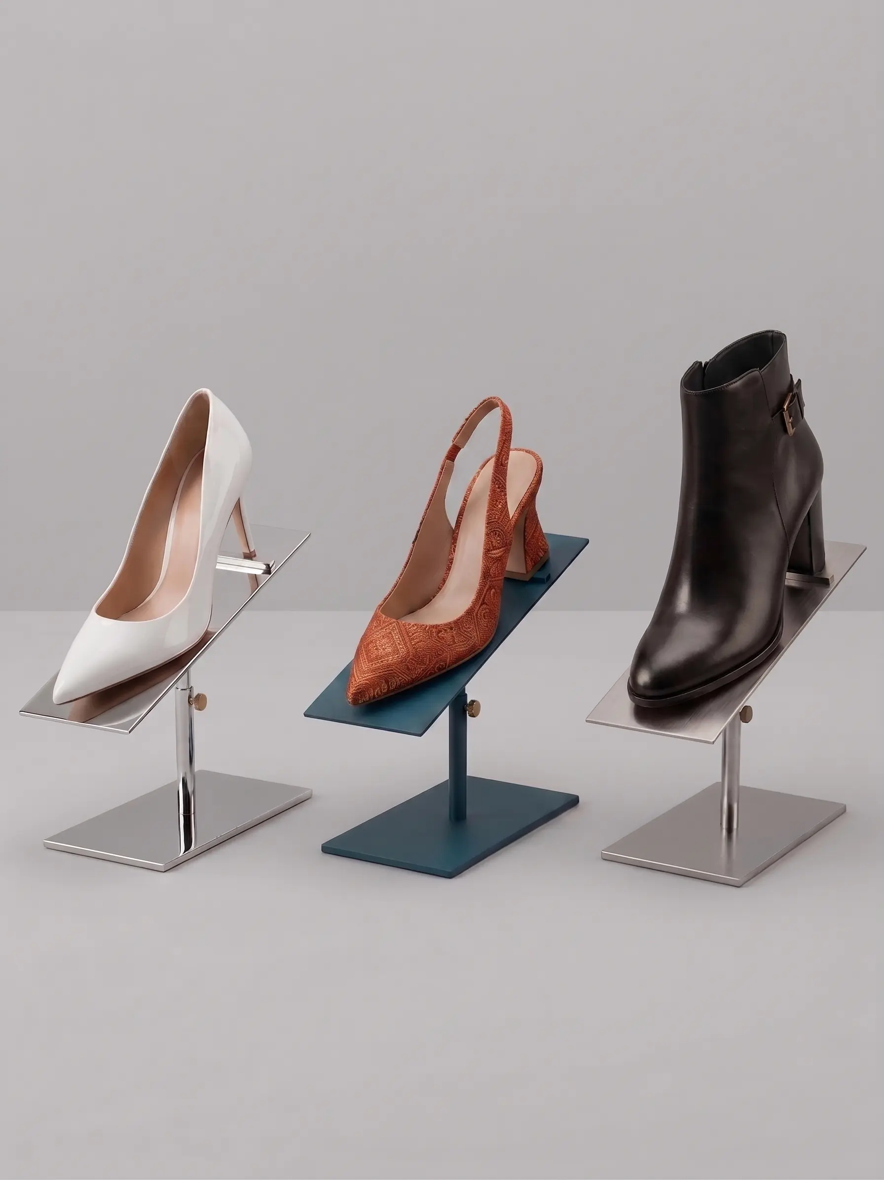 Tre paia di calzature presentate su supporti minimalisti inclinati in acciaio inossidabile