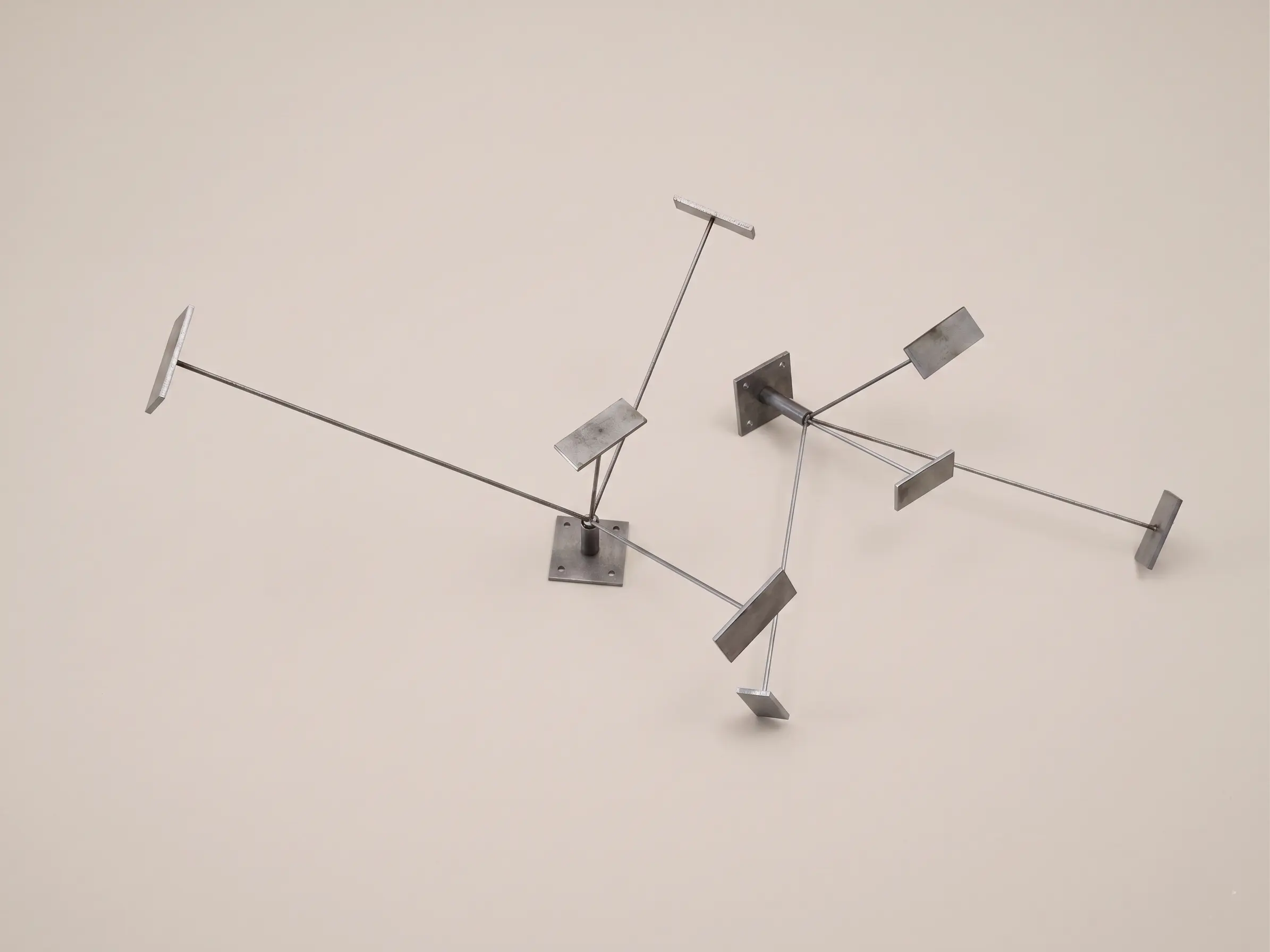 Two raw iron radial metal supports, composed of a square base and thin welded arms ending in small rectangular plates. Produced by DPEMME.