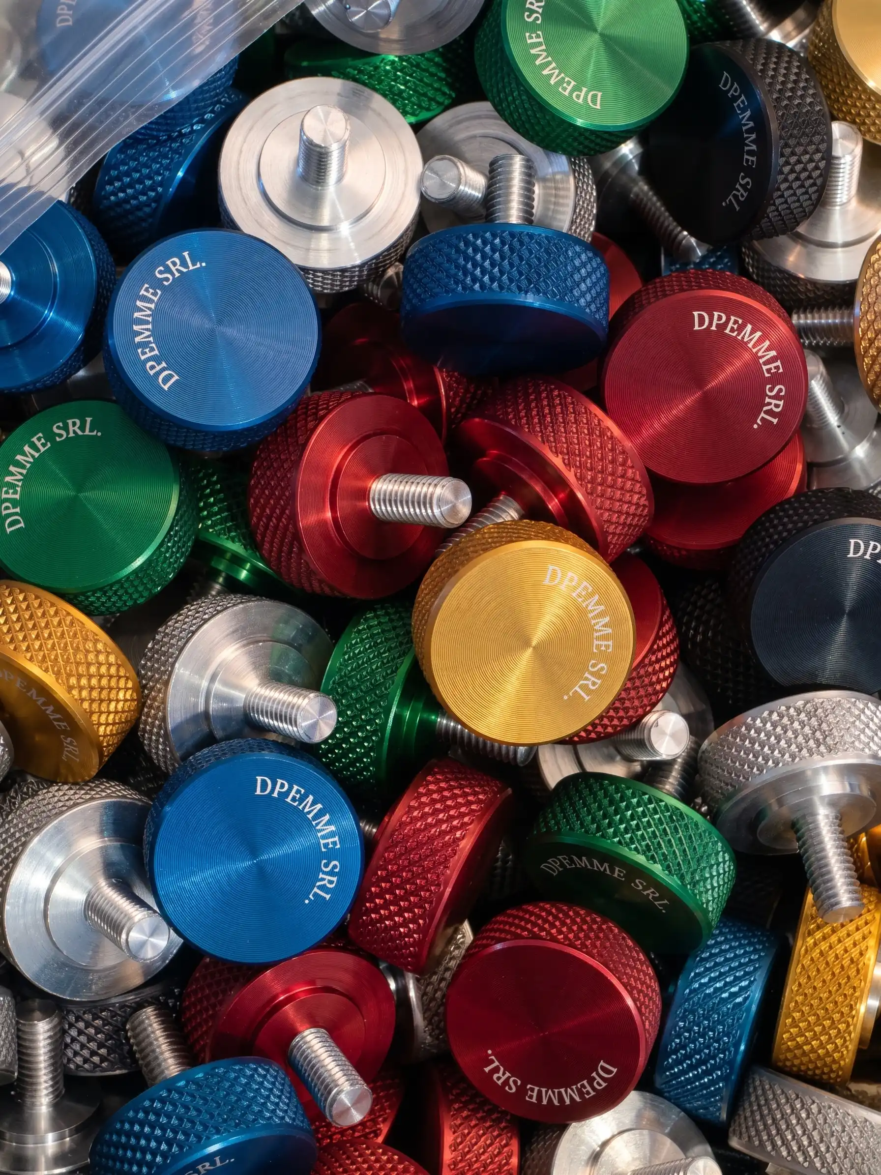 Insieme di pulsanti e manopole in alluminio lavorato, anodizzati in rosso, verde, blu, oro e nero, su uno sfondo scuro